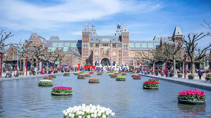 An old building with a gray roof and spires near a body of water with flowers