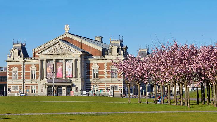 An old building with pillars and banners near grass and cherry blossom trees