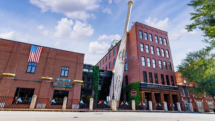 A red brick building with a large baseball bat sculpture under a blue sky with clouds