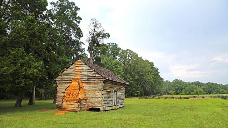 An old-fashioned log cabin sitting on the green grass next to trees