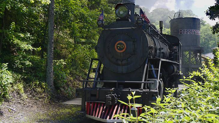 A black steam train with green trees and a wooden water tower in the background