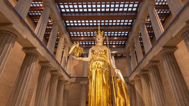 An englosed gold statue holding a winged goddess, a serpent, and a shield