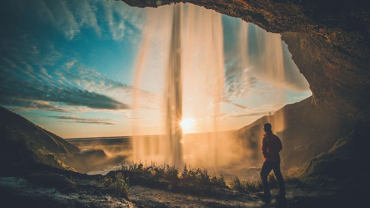 A man looking through mist from a waterfall cascading over a cliff