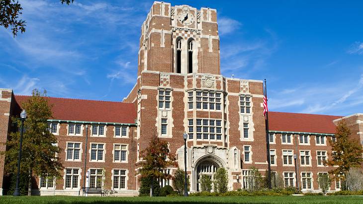 A large brown brick building with a tower clock, US flag, and black light posts