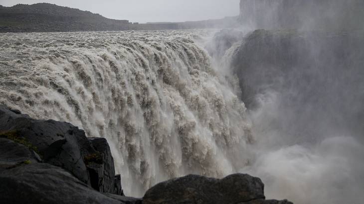 A very powerful grey waterfall gushing over a cliff's edge up close