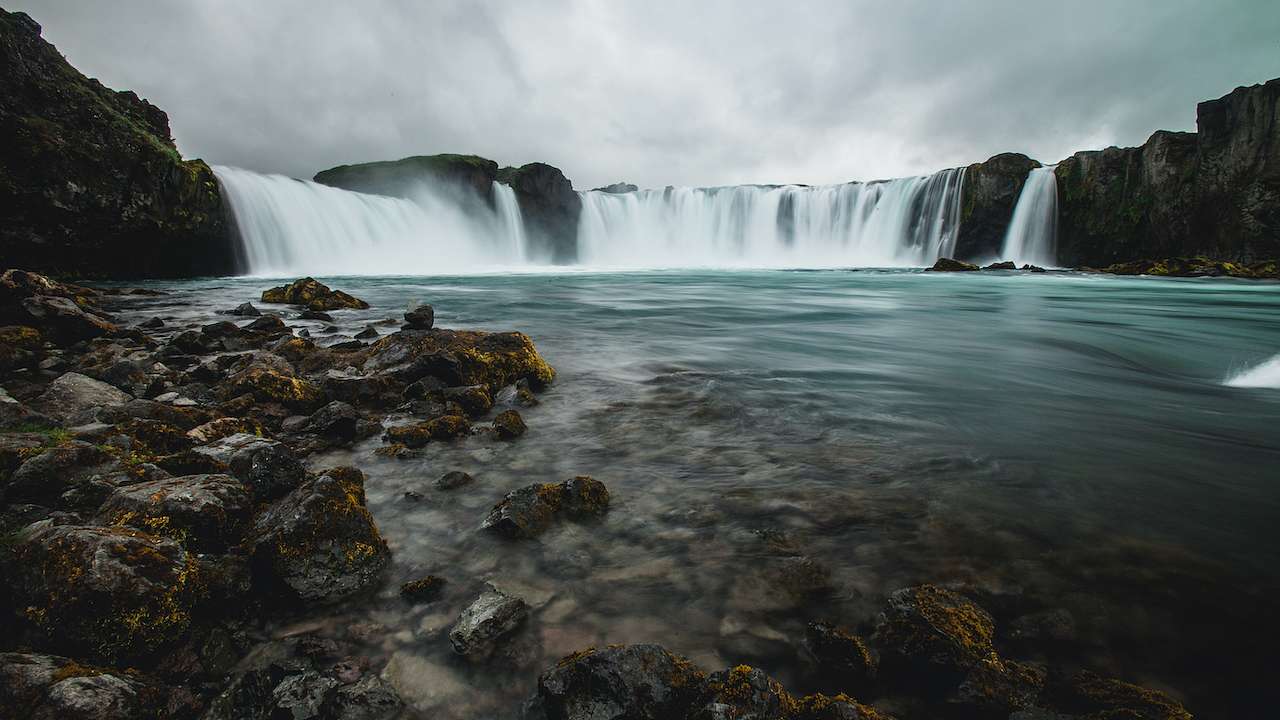 A semicircular waterfall plunging into turquoise blue water from the side