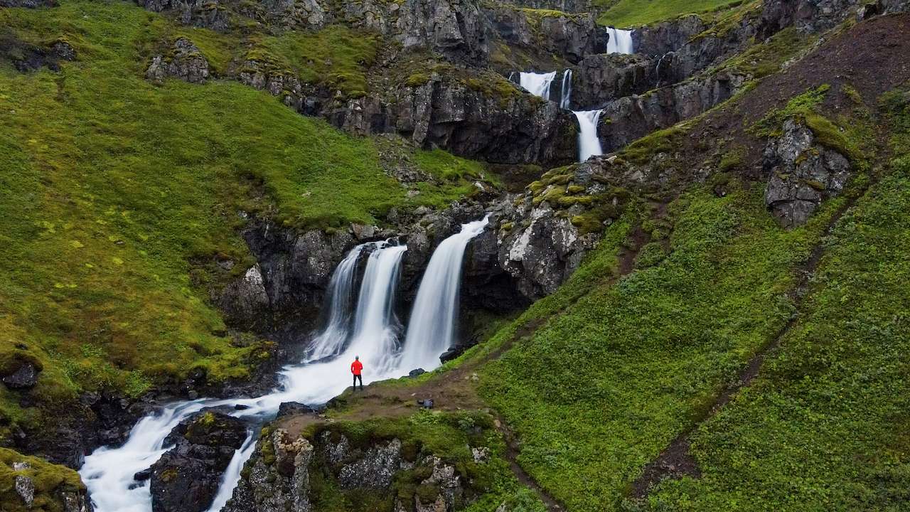 A set of cascading waterfalls down a rocky green hillside