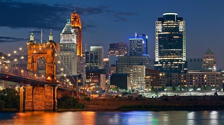 A view of an illuminated city next to a bridge and a river at night