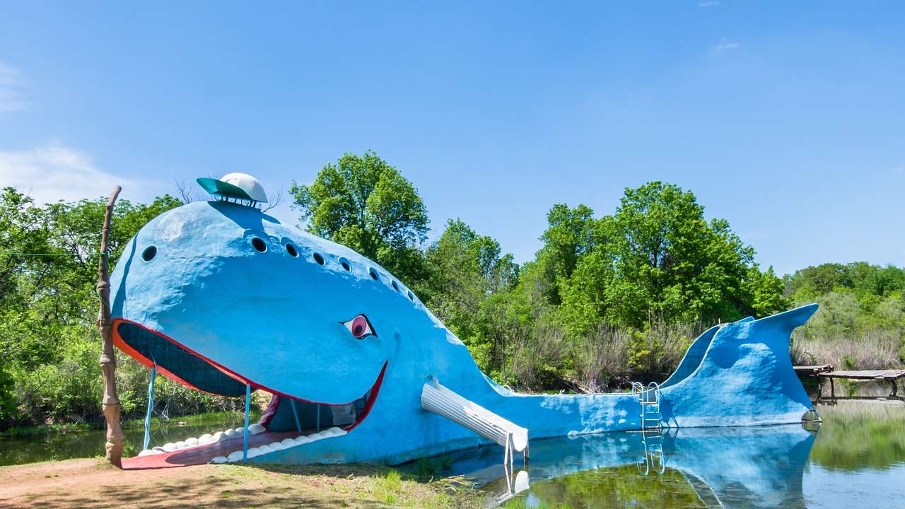 A large sculpture of a blue whale next to a pond and green trees
