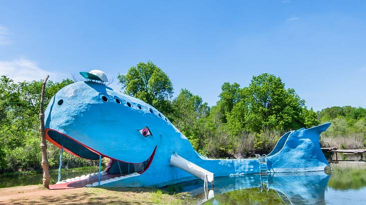 A large sculpture of a blue whale next to a pond and green trees