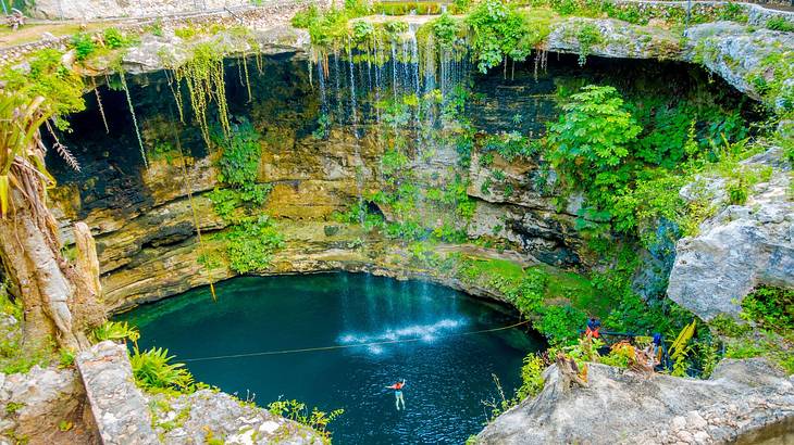 A sinkhole with blue water surrounded by rock walls with greenery on them