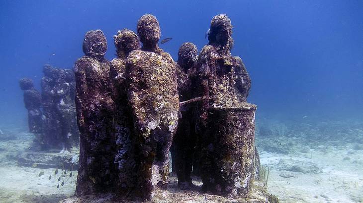 Groups of statues on the bottom of the ocean that are covered with algae