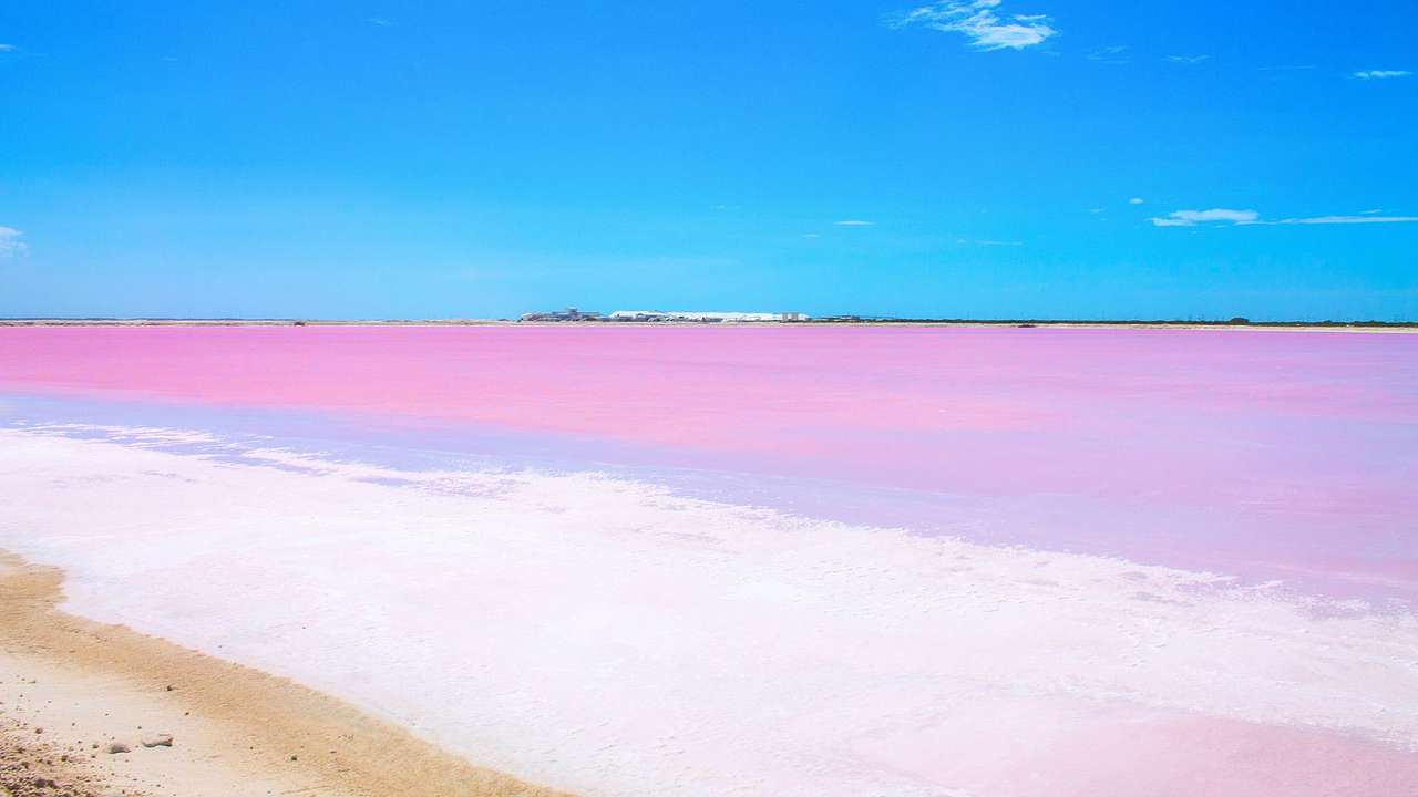 A pink lagoon with white sand to one side under a blue sky