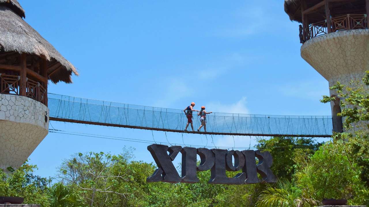 People walking across a bridge over the forest with an "Xplor" sign below