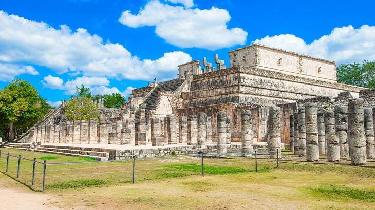 The ruins of a temple with a small fence around it and green grass on a nice day