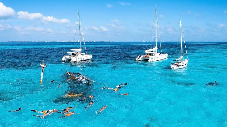People snorkeling around a shipwreck in clear waters with a few boats behind them