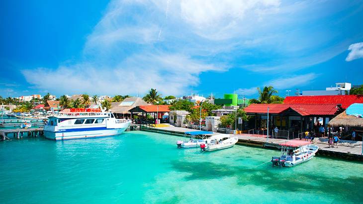 Boats moored on turquoise water next to small huts and green trees