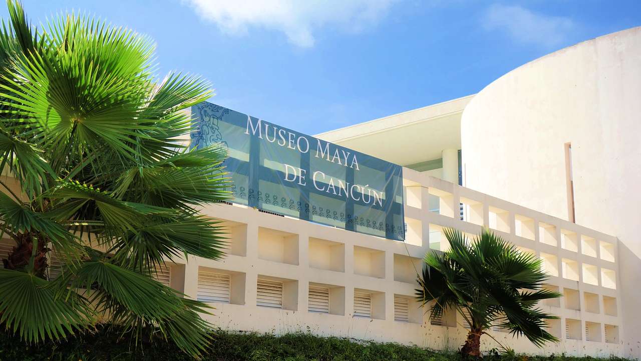 A building with a sign saying "Museo Maya De Cancún" next to greenery