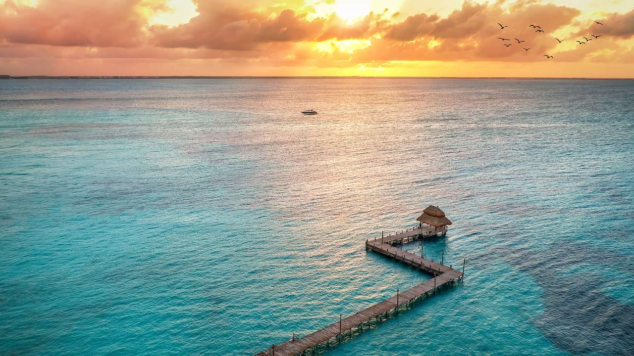 A wooden pathway leading to a hut in the middle of the ocean during sunset