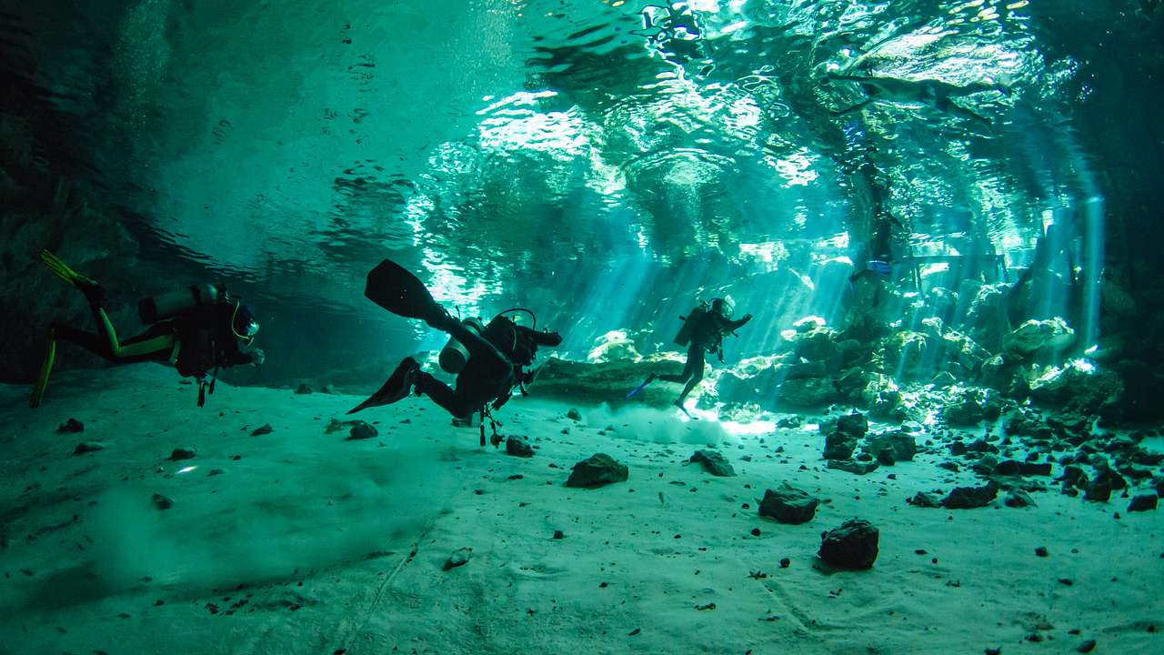 Sun rays passing through an underwater cave with divers exploring the area