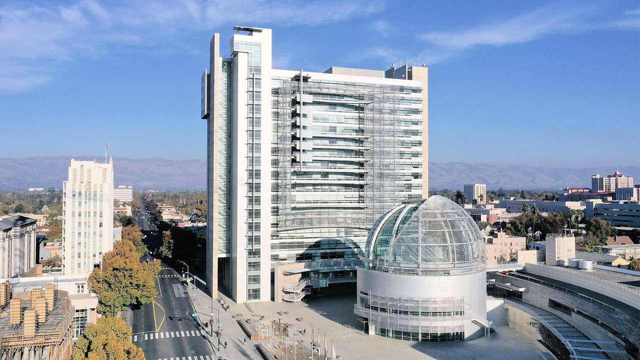 A gray modern building near a half-sphere-shaped building on a blue day