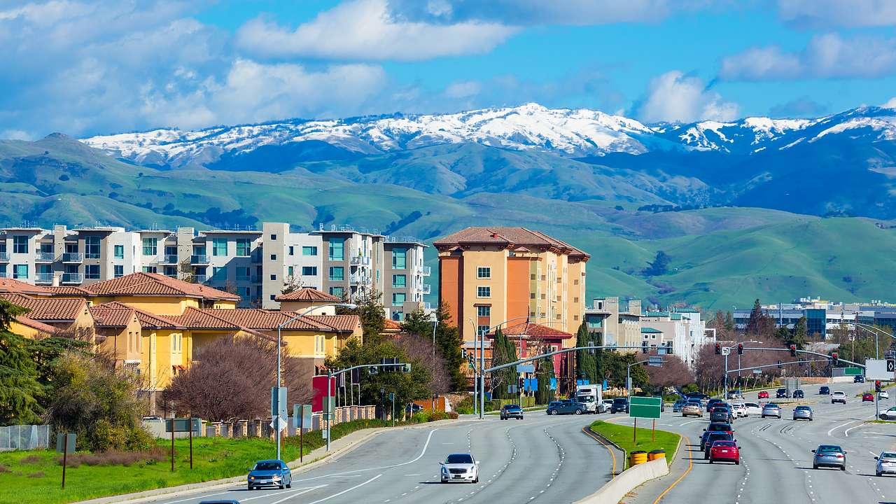 Cars on a highway near buildings, with snowcapped mountains in the background