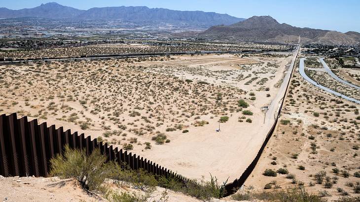 A long wall in the middle of a desert with mountains at the back