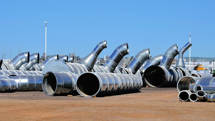 Large steel cylindrical pipes on the dirt ground with clear blue skies above