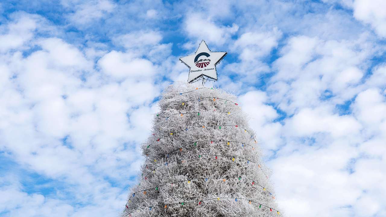 A white Christmas tree with a white star on top on a partly cloudy day