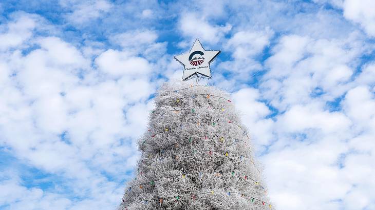 A white Christmas tree with a white star on top on a partly cloudy day