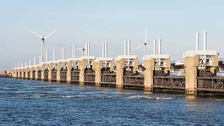 A dam with surge barriers over the water with wind turbines behind it