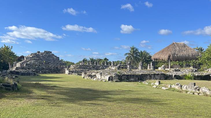 Green grass with ancient ruins and palm trees on it, on a partly cloudy day