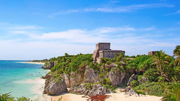 A beach with crystal water, rocky cliffs, and greenery under a blue sky