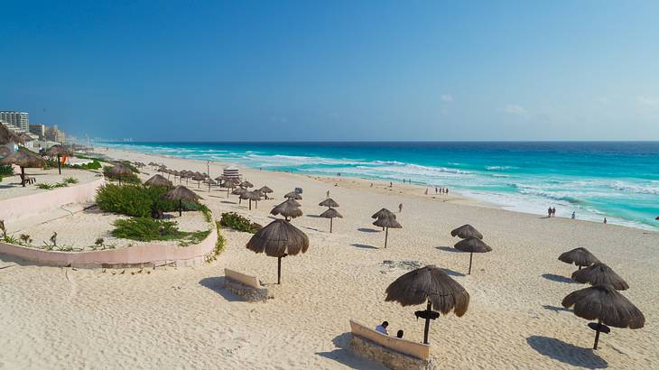 A beach with umbrellas and greenery and the ocean crashing onto the shore