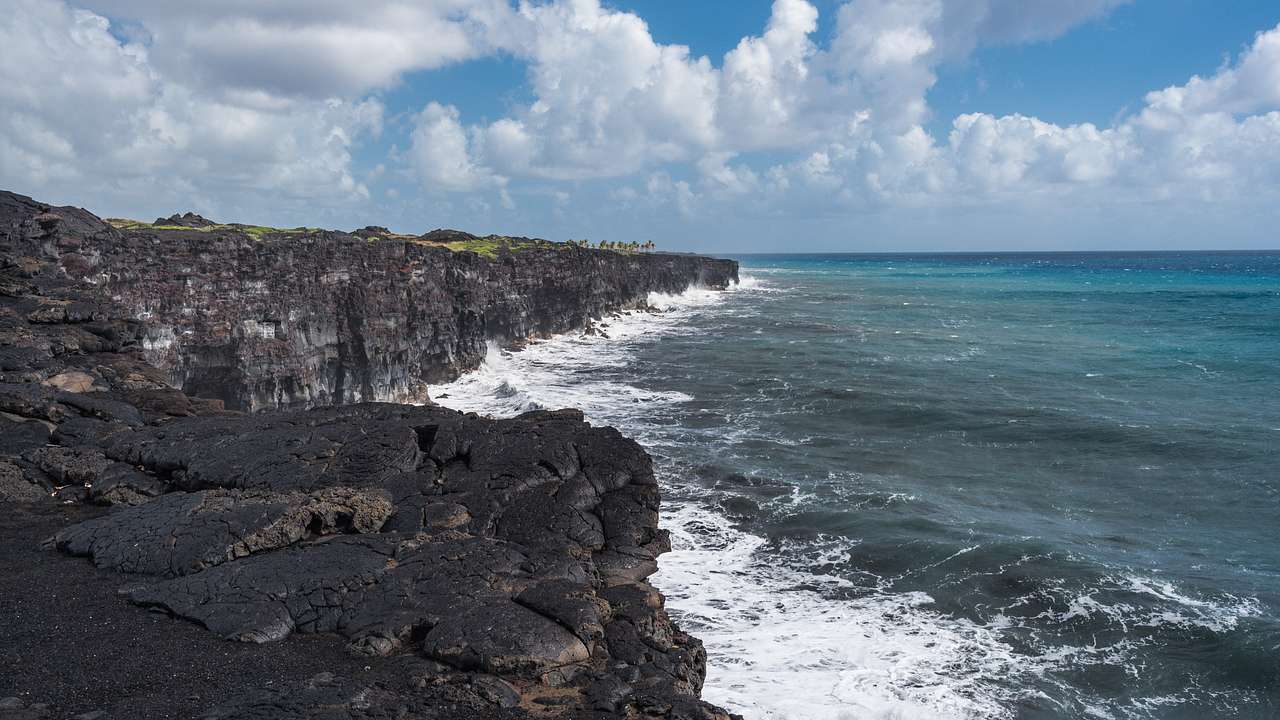 Ocean waves crashing on a rocky black volcanic coastline on a partly cloudy