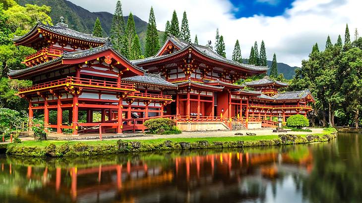 A red temple surrounded by greenery facing a body of water at the foot of a mountain
