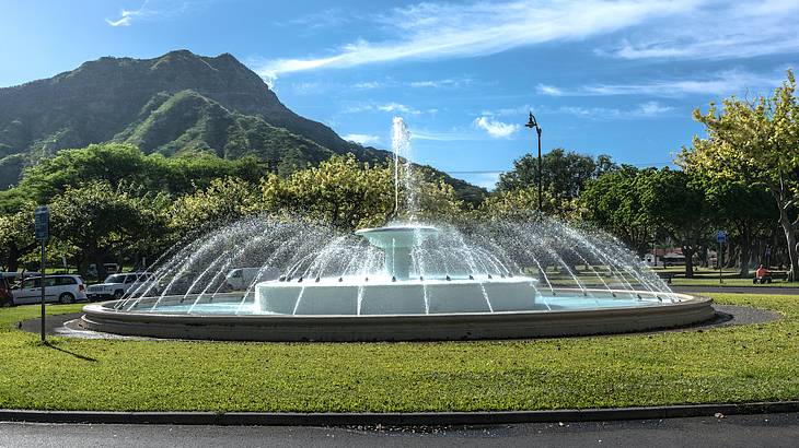 A fountain on a green lawn with a volcano in the background on a sunny day