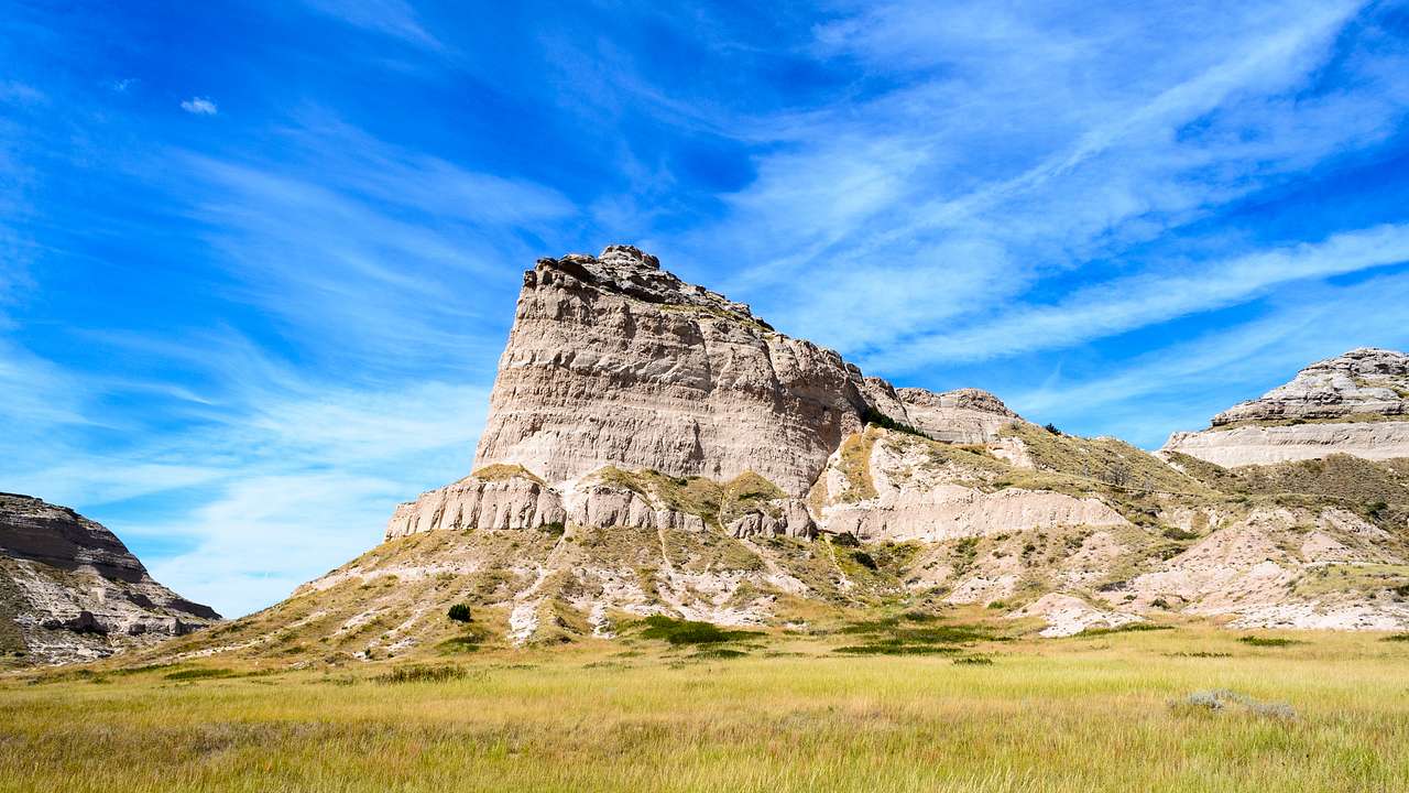 A steep layered rock formation with a grassland at its foot