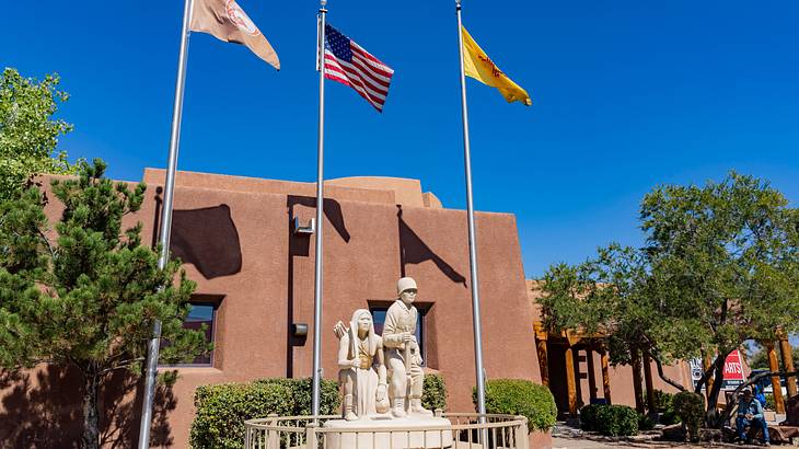 A pueblo structure with flagpoles and sculptures in front