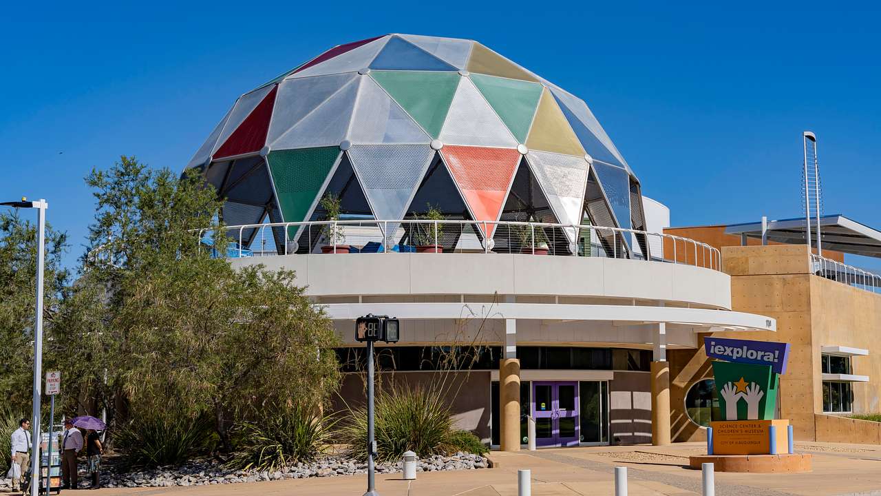 A dome-shaped building with colorful panels next to a path and a tree