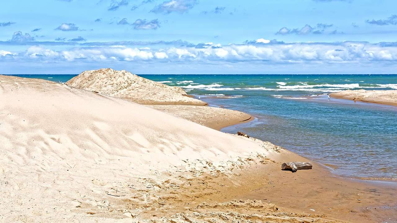 White sand dunes overlooking the blue water under a partly cloudy sky