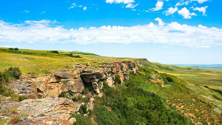 A rocky cliff surrounded by stunning green meadow and blue sky A rocky cliff surrounded by stunning green meadow and blue sky