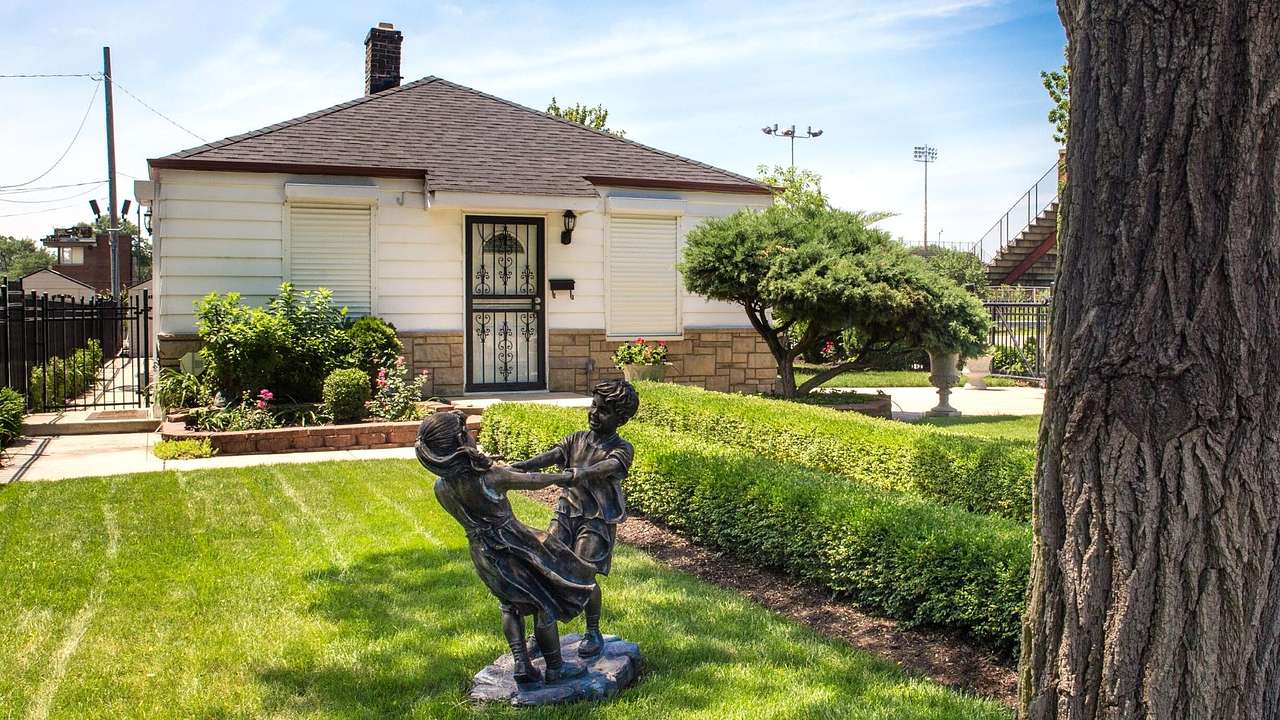 A statue of two kids playing on green grass against a white vernacular house
