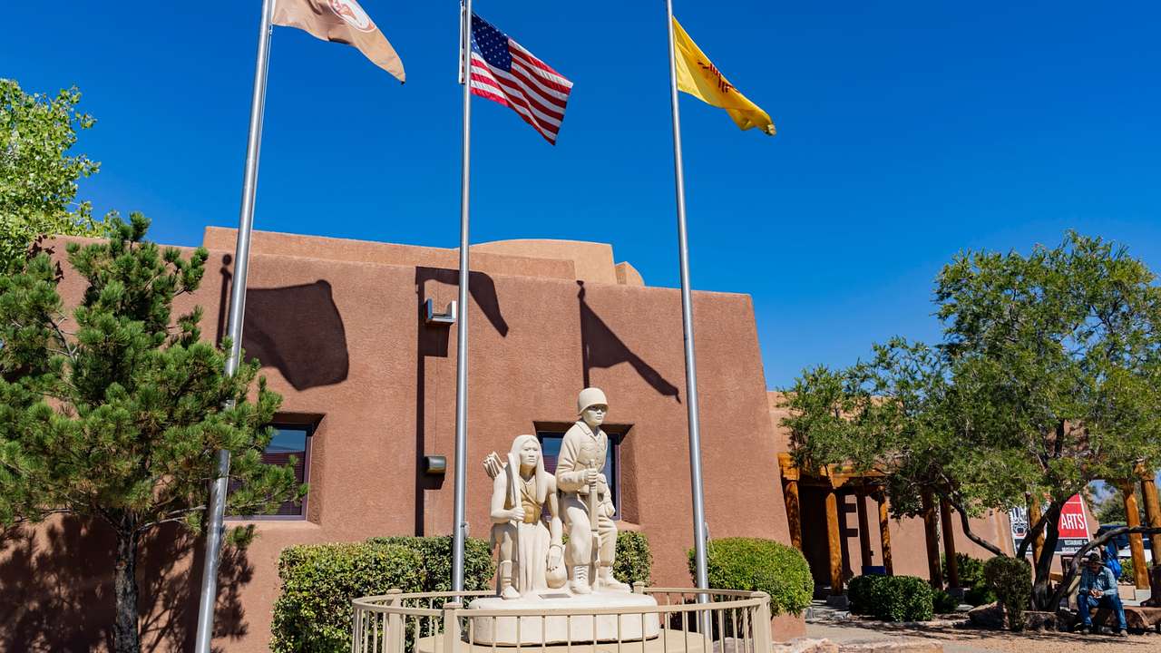 A small sculpture of two Indian Pueblos next to a sandstone building and three flags