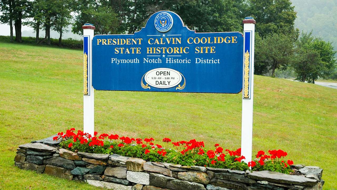 A blue sign on the grass that says "President Calvin Coolidge State Historic Site"