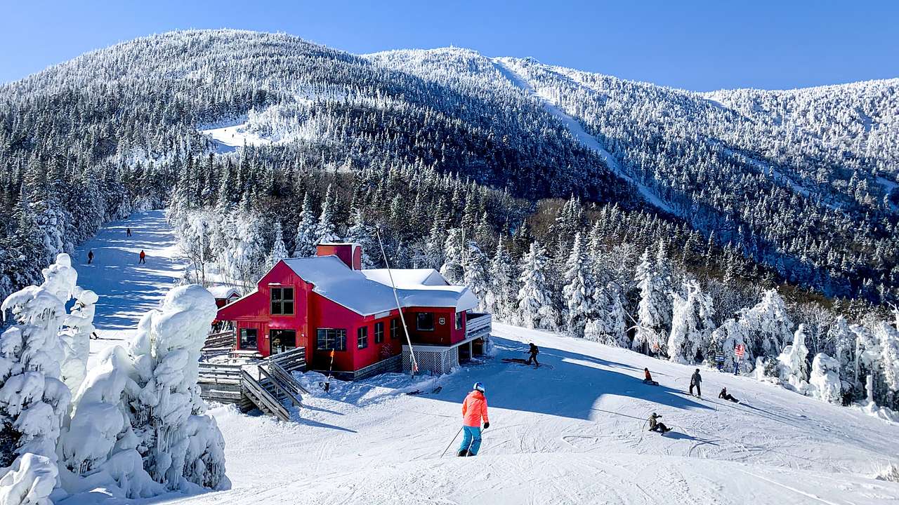 A snowy mountain with snow-covered trees, a red lodge, and people skiing
