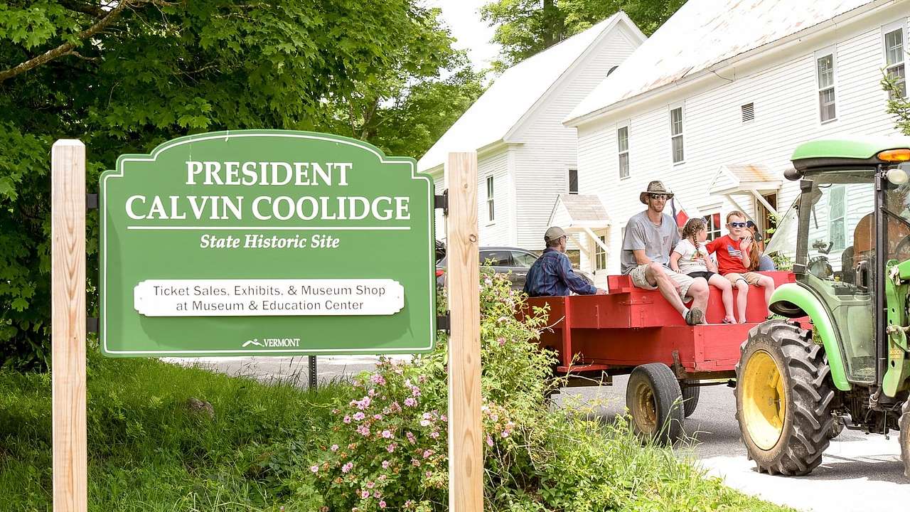 A green "President Calvin Coolidge State Historic Site" sign next to a tractor