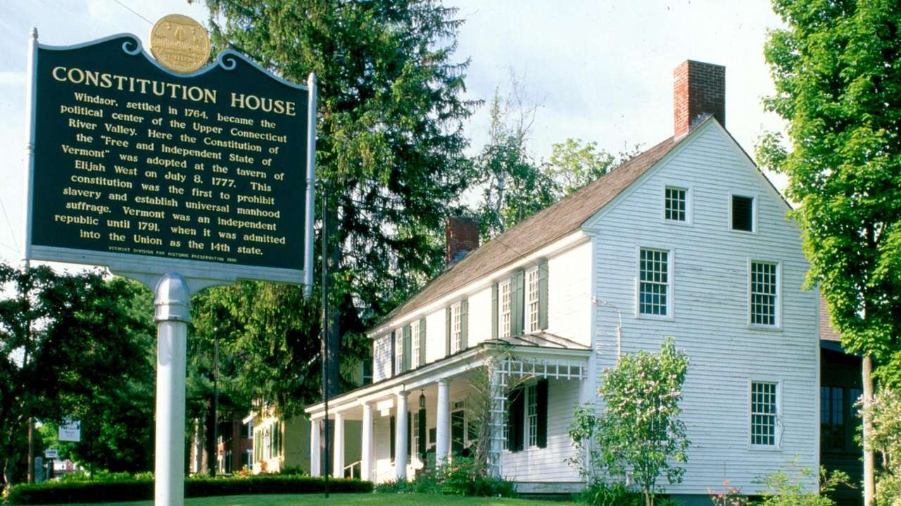 A white house and a green sign that says "Constitution House" with text below it