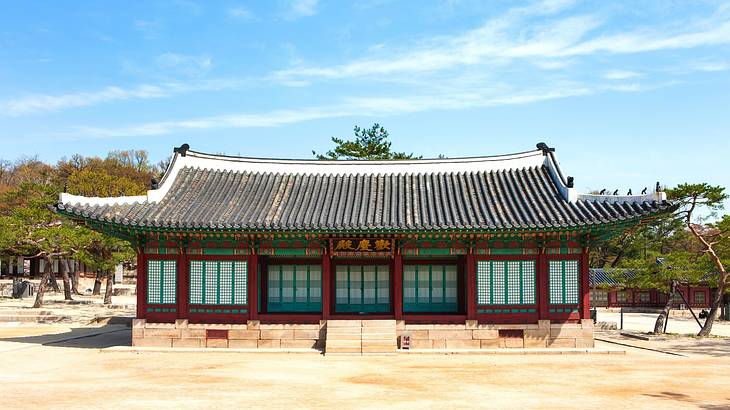 The outside of a Korean palace with trees in the back and blue sky above