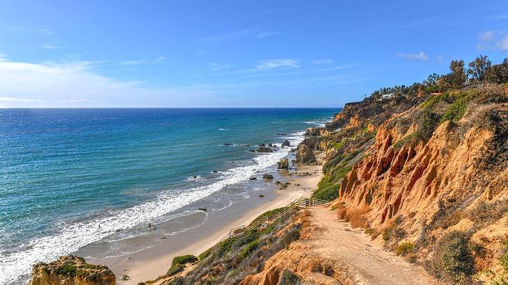 A coastline with ocean, sand, and small greenery-covered cliffs